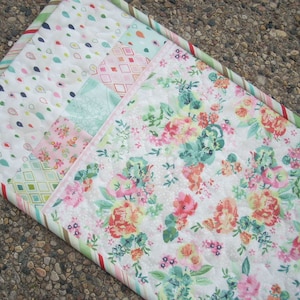 以下が含まれることがあります： ピンク、グリーン、ホワイトのフラワーパターンが施されたパッチワークキルト。キルトはストライプ、ドット、ダイヤモンドなど、さまざまなパターンを持つさまざまな生地で作られています。