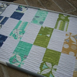 May include: A white quilt with a patchwork design featuring squares of various colors and patterns, including green, blue, yellow, and white. The quilt is made with a variety of fabrics, including floral prints, geometric patterns, and solid colors.