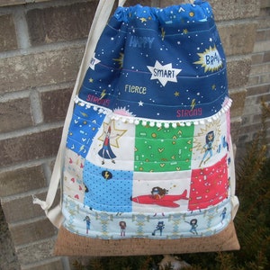 Może przedstawiać: Niebiesko-biały plecak ze sznurkiem i korkowym dnem. Plecak wykonany jest z tkaniny w patchworkowym wzorze z różnymi kolorami i wzorami. Tkanina ma nadrukowane słowa takie jak "Happy", "Smart", "Fierce" i "Strong".