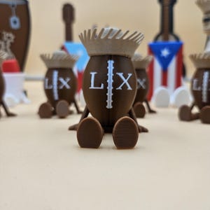 May include: Brown figurines with crown-like headwear and the letters "LX" on their bodies. The figurines have small, rounded feet and are arranged on a light-colored surface. Other decorative items, including a guitar-shaped object and a drum, are visible in the background.
