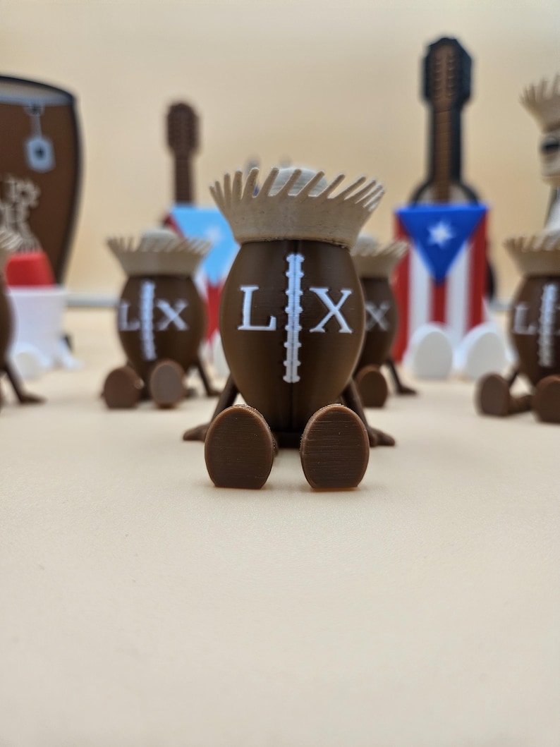 May include: Brown figurines with crown-like headwear and the letters "LX" on their bodies. The figurines have small, rounded feet and are arranged on a light-colored surface. Other decorative items, including a guitar-shaped object and a drum, are visible in the background.