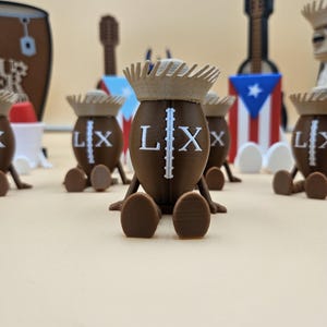 May include: A collection of brown, football-shaped figurines with the letters "LX" and a vertical line printed on them. Each figurine has a light brown crown and is sitting down. In the background are miniature guitars and a Puerto Rican flag.