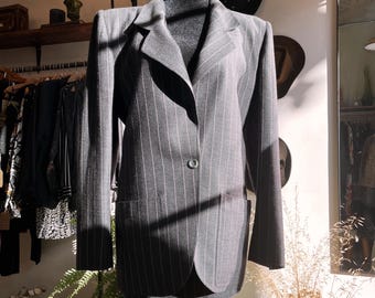 May include: A dark gray blazer with a pinstripe pattern, displayed on a mannequin. The blazer has a single-button closure, notched lapels, and two front pockets. The garment is part of a vintage clothing collection.