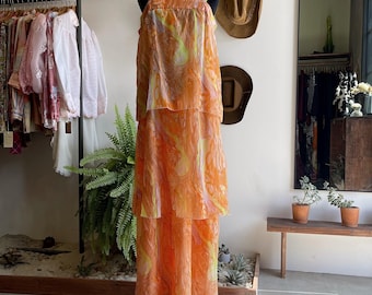 May include: A long, tiered maxi dress with a marbled pattern in shades of orange, yellow, and white. The dress has a sleeveless design and a square neckline.