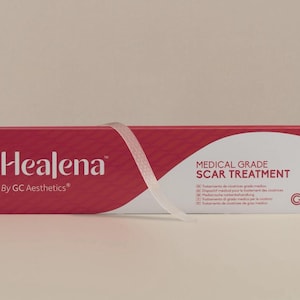 Può includere: Una scatola rossa e bianca di trattamento delle cicatrici di grado medico Healena. La scatola ha il nome del marchio e le informazioni sul prodotto stampate in bianco. Un nastro trasparente è avvolto attorno alla scatola.