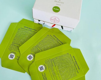 May include: A white box with the text "HEALTH & BEAUTY SHOP" and a green circle sticker. Three green packets with the text "DETOX REVOLUTION" and instructions are in the foreground. The packets have a QR code.