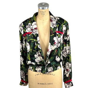 May include: A long-sleeved jacket featuring a dark background with a white and green floral pattern. The jacket has a notched collar, a single button closure, an elasticized waist, and red trim accents on the shoulders and sleeve cuffs.