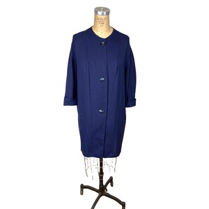 Può includere: Un cappotto blu navy vintage con tre bottoni e maniche a tre quarti. Il cappotto è esposto su un manichino con un supporto in metallo. Il cappotto ha un design semplice e classico.