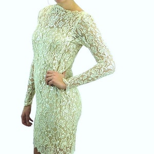May include: A cream-colored lace dress with long sleeves and a knee-length hemline. The dress features an intricate floral pattern and a high neckline. The dress is form-fitting and appears to be made of a delicate fabric.