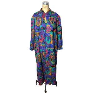 May include: A long-sleeved, floor-length robe featuring a vibrant, multi-colored geometric and abstract pattern in shades of blue, purple, teal, pink, and yellow. The garment has a high collar, a front zipper closure, and a small yellow tassel pull.
