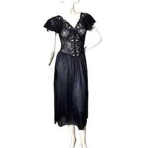 May include: Black vintage dress with a lace bodice and short sleeves. The dress has a V-neckline and a flowing skirt. The dress is displayed on a mannequin.