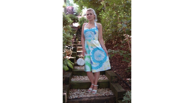 May include: A knee-length halter dress featuring a white base with a vibrant floral pattern in shades of bright blue and lime green. The dress has a sweetheart neckline, a fitted bodice, and a flared skirt, paired with white ankle-strap sandals.
