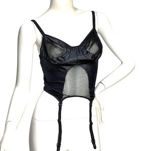 May include: A black bustier top featuring a satin-like finish, mesh panels on the cups, and a large central mesh cutout. The garment includes adjustable shoulder straps and two attached garter straps with metal clips hanging from the bottom hem.