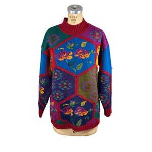 Puede incluir: Un suéter vintage de patchwork con cuello alto. El suéter presenta una vibrante mezcla de colores, incluyendo rojo, azul, verde, morado y amarillo. Los diseños florales están incorporados en el diseño, agregando un toque de fantasía a la prenda.
