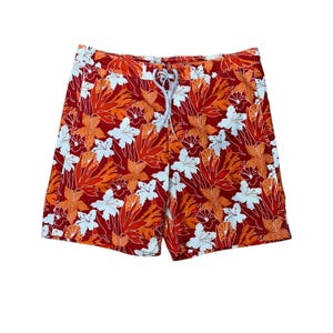 May include: Board shorts featuring a vibrant floral pattern in shades of red, orange, and white. The shorts have an elasticized waistband with a white drawstring closure at the center front, providing a secure fit for swimming or casual wear.