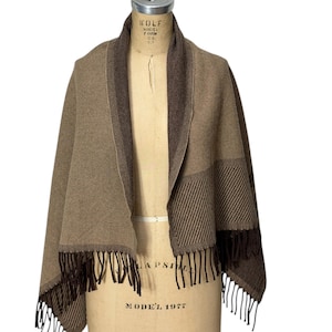 May include: A brown and tan shawl with a fringed hem. The shawl is draped over a mannequin. The shawl has a dark brown collar and a striped pattern on the lower portion of the shawl.