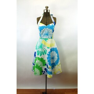 May include: A knee-length halter dress featuring a white base with a vibrant floral pattern in shades of bright blue, lime green, and pale yellow. The dress has a sweetheart neckline, a fitted bodice, and a flared skirt with a defined waistline.