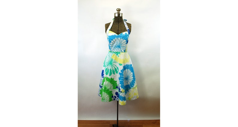 May include: A knee-length halter dress featuring a white base with a vibrant floral pattern in shades of bright blue, lime green, and pale yellow. The dress has a sweetheart neckline, a fitted bodice, and a flared skirt with a defined waistline.
