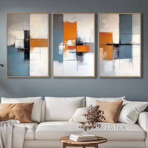 May include: Three abstract paintings with geometric shapes in shades of white, gray, orange, and black. The paintings are framed in a light wood frame and are hung on a gray wall above a white sofa.