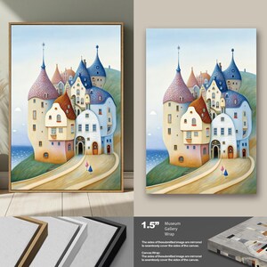 May include: A framed canvas print featuring a whimsical illustration of a village on a hill overlooking the sea. The buildings have colorful roofs and unique architectural details. The artwork is set against a blue sky and a light brown frame.