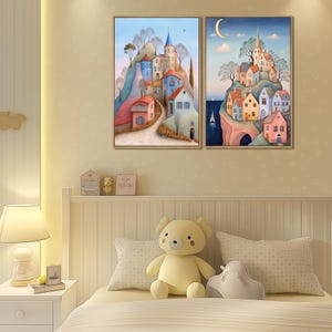 May include: Two framed landscape paintings. One depicts a village on a hill with blue, red, and white buildings. The other shows a similar village under a crescent moon. Both have a whimsical, storybook style.