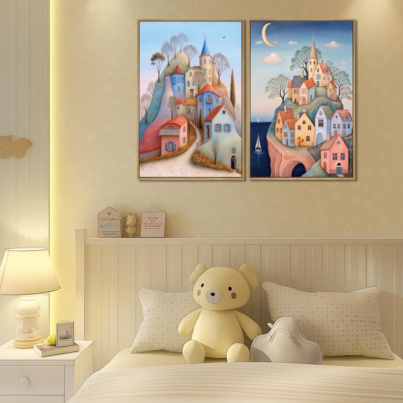 May include: Two framed landscape paintings. One depicts a village on a hill with blue, red, and white buildings. The other shows a similar village under a crescent moon. Both have a whimsical, storybook style.