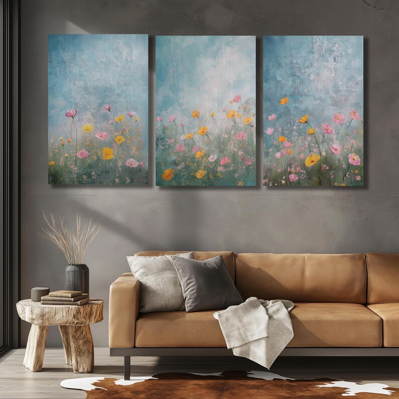 K&ouml;nnte beinhalten: Ein dreiteiliges Wandbild-Set aus Leinwand mit einer Aquarellmalerei eines Feldes mit rosa und gelben Blumen vor blauem Hintergrund.