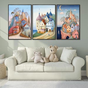May include: Three framed watercolor paintings depict whimsical villages on hillsides with colorful buildings, trees, and a crescent moon. The paintings are displayed above a white sofa with stuffed animals.