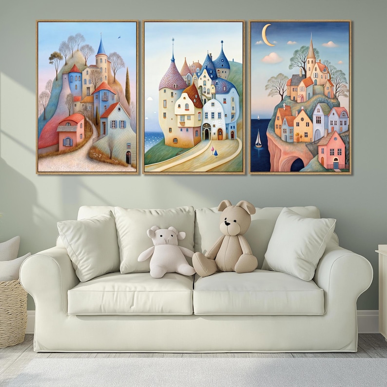 May include: Three framed art prints depicting whimsical village scenes with colorful buildings, set against a backdrop of blue skies and rolling hills. The artwork is displayed above a white sofa with teddy bears.