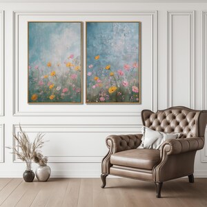K&ouml;nnte beinhalten: Zwei gerahmte Bilder mit einem Feld aus rosa und gelben Blumen vor einem blauen und wei&szlig;en Hintergrund. Die Bilder h&auml;ngen an einer wei&szlig;en Wand &uuml;ber einem braunen Ledersessel.