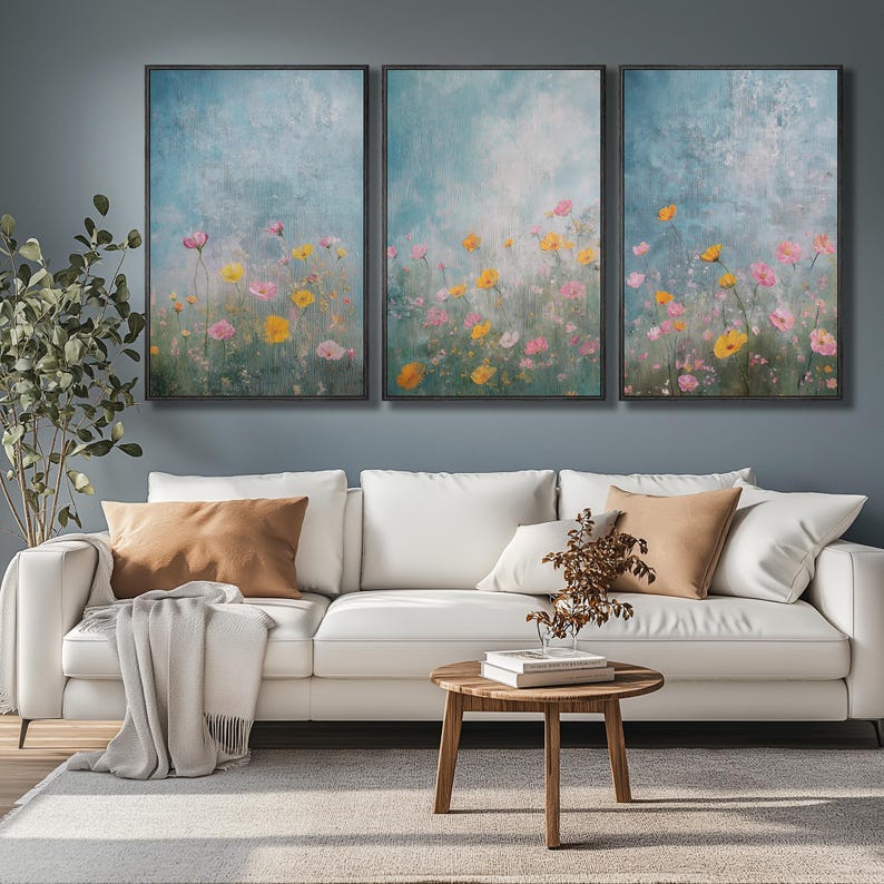 K&ouml;nnte beinhalten: Drei gerahmte Leinwanddrucke mit einem Aquarell-Stil-Gem&auml;lde eines Feldes mit rosa und gelben Blumen vor einem blauen und wei&szlig;en Hintergrund.