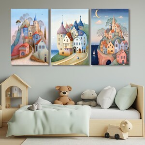 May include: Three canvas art prints depicting whimsical European villages. The artwork features colorful buildings, winding roads, and a serene landscape. The paintings are displayed above a child's bed with a wooden frame and soft toys.