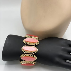 May include: A gold bracelet with five oval-shaped pink stones. The bracelet is on a black mannequin arm.
