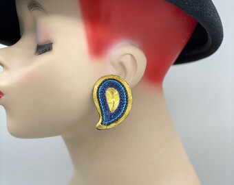 May include: A pair of gold and blue paisley-shaped earrings. The earrings are made of metal and have a textured surface.
