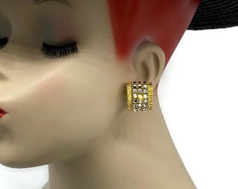 May include: Gold tone clip-on earrings with clear rhinestones. The earrings are rectangular in shape and have a geometric design.