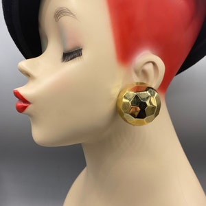 May include: A pair of gold-toned geometric earrings. The earrings are large and round, with a faceted design.
