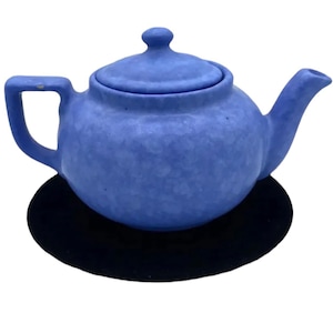 May include: A blue ceramic teapot with a lid, sitting on a black coaster. The teapot has a textured surface and a rounded body.