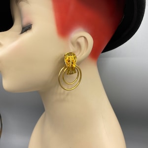 May include: Gold tone hoop earrings with a textured, abstract design. The earrings have three hoops.