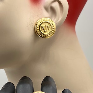 Puede incluir: Conjunto de anillo y pendientes de tono dorado con un diseño circular con las letras "NY" en el centro. El anillo y los pendientes tienen un borde texturizado con forma de cuerda.