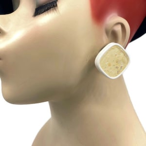 May include: A pair of white square earrings with a gold flecked design.