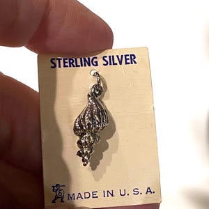 May include: Sterling silver seashell charm on a white card with blue text that reads "STERLING SILVER" and "MADE IN U.S.A."