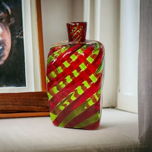 May include: A red and green glass bottle with a swirl design. The bottle has a wide mouth and a narrow neck.