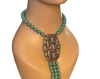 May include: A turquoise beaded necklace with a large, ornate pendant featuring a gold-tone design and colorful rhinestones.
