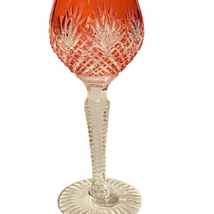 Könnte beinhalten: Ein hohes, klares Glas mit einer roten, geschliffenen Schale und einem klaren, geschliffenen Stiel und Fuß.