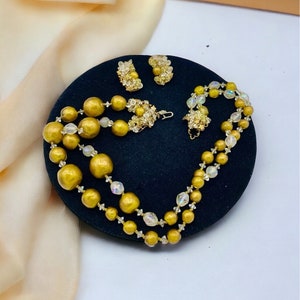 Peut inclure: Un collier en or avec de grosses perles rondes et de petites perles transparentes. Le collier est assorti à des boucles d'oreilles en or avec des pierres transparentes.
