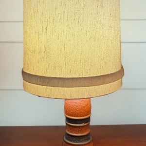 May include: A vintage table lamp with a brown and orange ceramic base and a beige fabric lampshade.