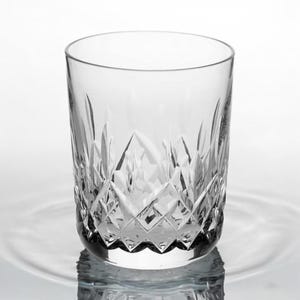 Puede incluir: Un vaso de cristal transparente con un dise&ntilde;o de cristal tallado. El vaso est&aacute; vac&iacute;o y se encuentra sobre una superficie blanca.