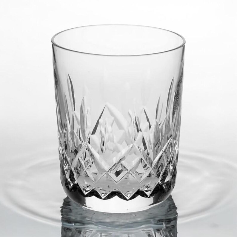 Puede incluir: Un vaso de cristal transparente con un dise&ntilde;o de cristal tallado. El vaso est&aacute; vac&iacute;o y se encuentra sobre una superficie blanca.