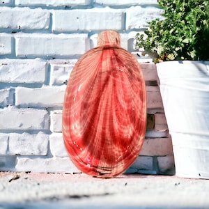 Può includere: Una bottiglia decorativa in vetro con un design a righe rosse e bianche. La bottiglia ha una forma arrotondata e un collo piccolo. La bottiglia è esposta davanti a un muro di mattoni bianchi.