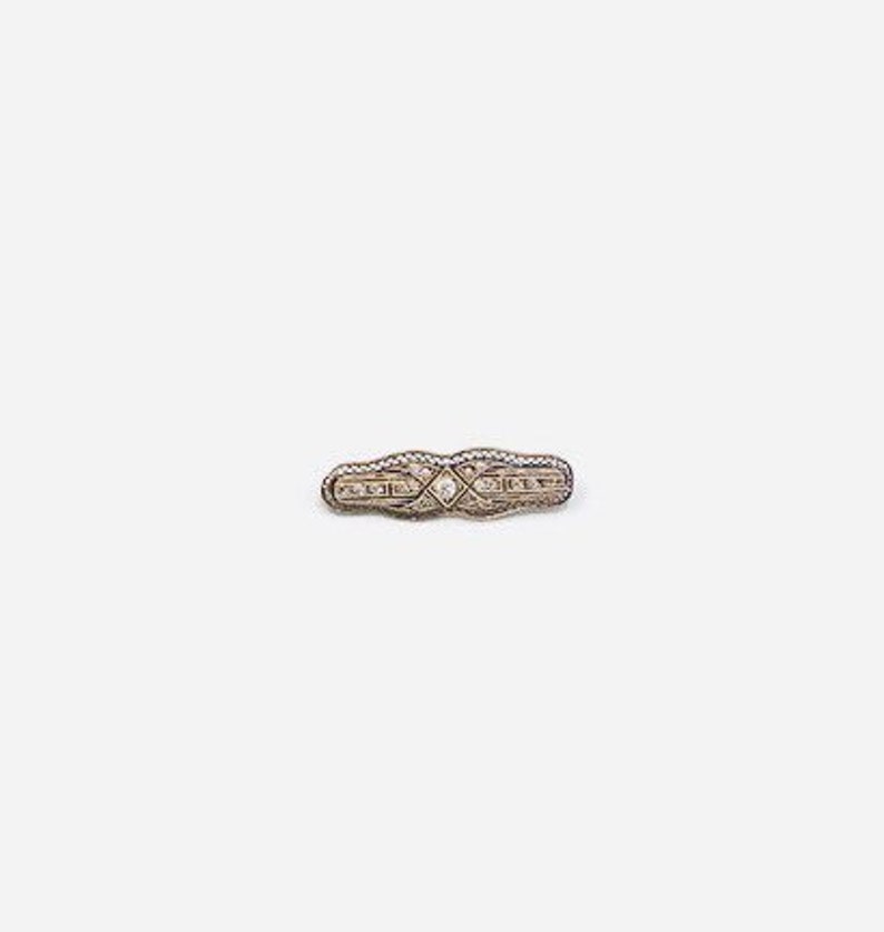 May include: A silver brooch with a diamond-shaped design and small clear stones.
